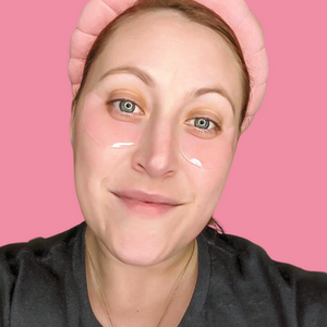 Woman smiling wearing Hydrating Reusable Under Eye Patches | Dreambox Beauty on her under eyes against a pink background in a skincare and wellness context.