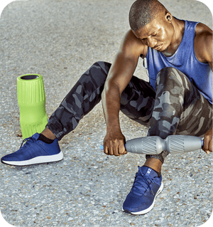 Man using a recovery tool on his calf outdoors next to a green foam roller, demonstrating the RAD Muscle Flushing Kit | RAD for muscle recovery and wellness.
