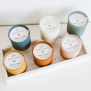 Oakmoss + Amber Dignity Series Glass Jar Soy Candle | Calyan Wax Co. - 5.3 oz displayed among five other assorted scented candles in colorful glass jars on a white tray.