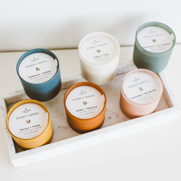 Oakmoss + Amber Dignity Series Glass Jar Soy Candle | Calyan Wax Co. - 5.3 oz displayed among five other assorted scented candles in colorful glass jars on a white tray.