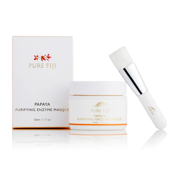 Papaya Purifying Enzyme Masque | Pure Fiji in a white jar with gold accents alongside its matching box and a white silicone applicator brush for skincare and body care wellness.