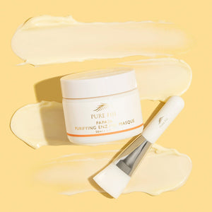 A jar of Papaya Purifying Enzyme Masque | Pure Fiji with a white applicator brush resting on a smooth, creamy pale yellow skincare masque texture background.