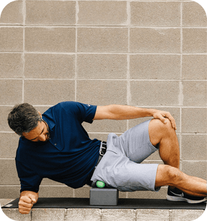 Man using RAD Rounds - 3 Set | RAD green recovery tool under his hip while lying on his side on a yoga mat in front of a brick wall for body care and wellness.