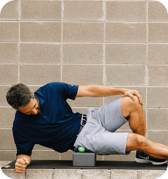 Man using RAD Rounds - 3 Set | RAD green recovery tool under his hip while lying on his side on a yoga mat in front of a brick wall for body care and wellness.