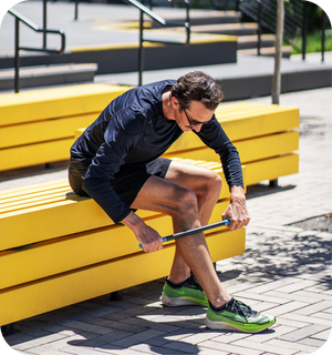 Man using RAD ROD | RAD muscle recovery tool on his calf while seated on a bright yellow bench outdoors in athletic wear.