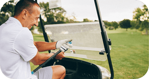 Man sitting in a golf cart on a sunny day outdoors holding a wellness recovery tool named RAD ROD | RAD, designed for muscle relief and body care.