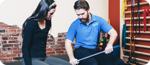 Man demonstrating a recovery tool called RAD ROD | RAD to a woman in a wellness or therapy setting with exercise equipment in the background.