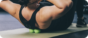 Person using a green RAD Roller Soft | RAD massage tool under their upper back while lying on a yoga mat, demonstrating muscle recovery and wellness care.