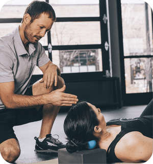 A man guides a woman using the RAD Roller Soft | RAD for targeted muscle recovery and body care, demonstrating its use on her upper back and neck in a wellness setting.
