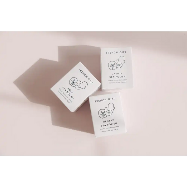 Three minimalist French Girl skincare product boxes in soft natural light, featuring Rose Body Polish | French Girl along with Jasmin and Menthe Sea Polish varieties.
