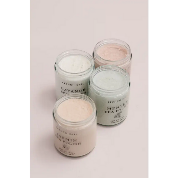Four glass jars of French Girl skincare polishes in soft pastel colors, including Rose Body Polish | French Girl, arranged on a pale background for body care and wellness.