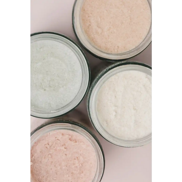 Close-up of four glass jars filled with textured natural body scrubs in soft pastel shades, featuring Rose Body Polish | French Girl for skincare and body care.