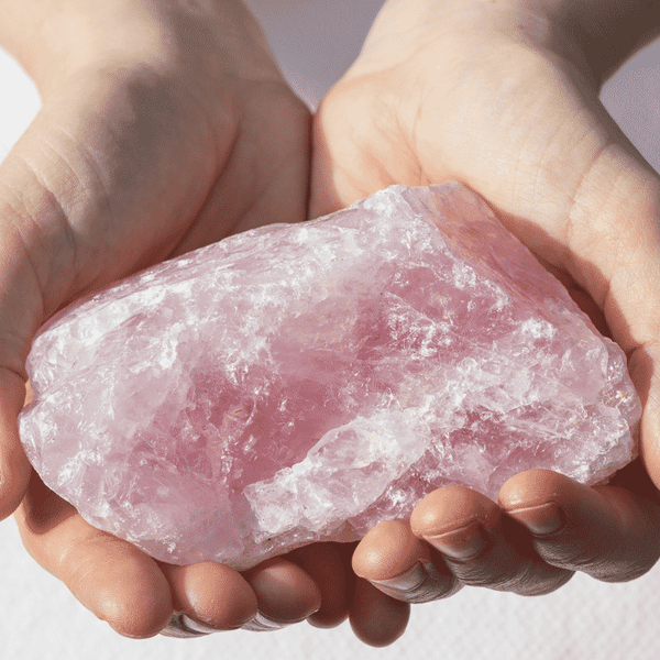 Hands gently holding a large pink rose quartz crystal, highlighting the natural stone linked to the Gentle Mineral Toner - Infused w/ Rose Quartz | Privai for skincare and wellness.