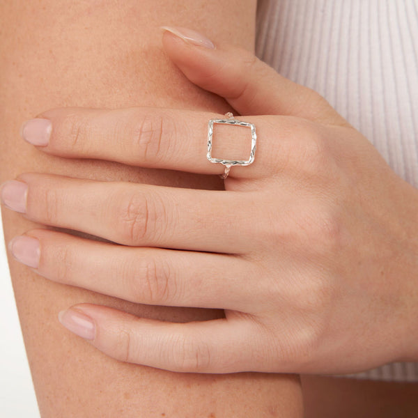 Close-up of a hand wearing the Geometry Square Ring | Little Sparkles with a delicate, textured square design in silver, resting on a light skin tone against a neutral background.