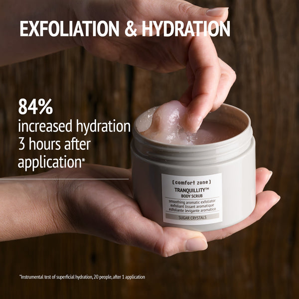 Hand holding an open jar of [ comfort zone ] Tranquillity body scrub with a fingertip scooping the exfoliating cream, highlighting exfoliation and hydration benefits of Kit Secret Garden | [ comfort zone ].