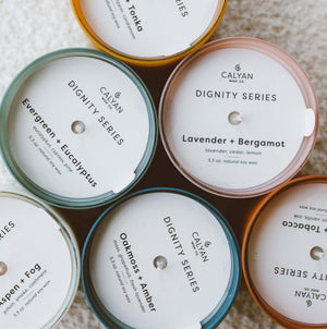 Vetiver + Tonka Dignity Series Glass Jar Soy Candle | Calyan Wax Co. - 5.3 oz displayed among other scented candles arranged in a circle on a soft surface.
