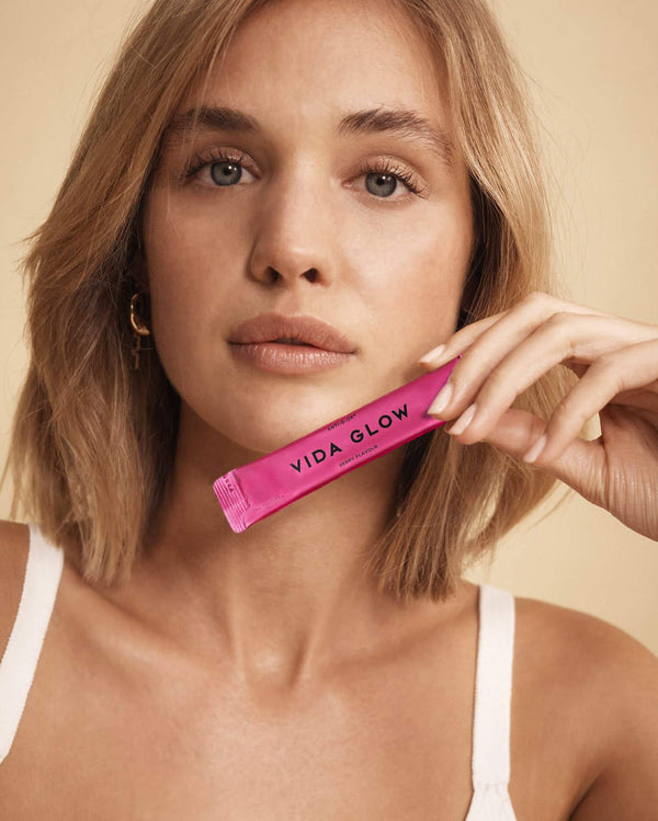 Woman with natural makeup holding a pink sachet labeled Anti-G-Ox Berry | VIDA GLOW, promoting skincare and wellness supplements for vibrant skin.