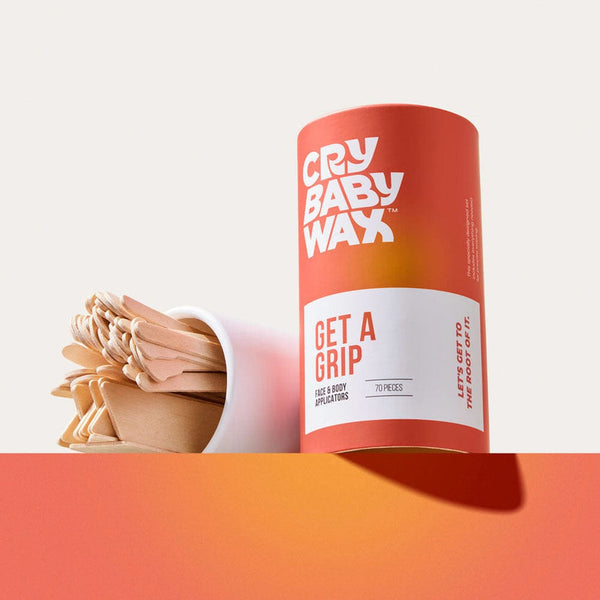 Container of Get a Grip Face & Body Applicators | Crybaby Wax with wooden applicators spilling from a white cup on a warm gradient surface for skincare and body care use.