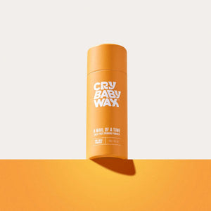 A bright orange cylindrical container of A Wail of a Time Priming Powder | Crybaby Wax standing upright on an orange surface against a light background, designed for skincare and body care.