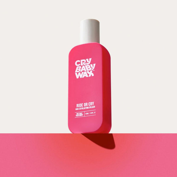 Bright pink bottle of Ride or Cry AHA Exfoliating Splash | Crybaby Wax with white cap on a matching pink surface, showcasing skincare product packaging for exfoliation.
