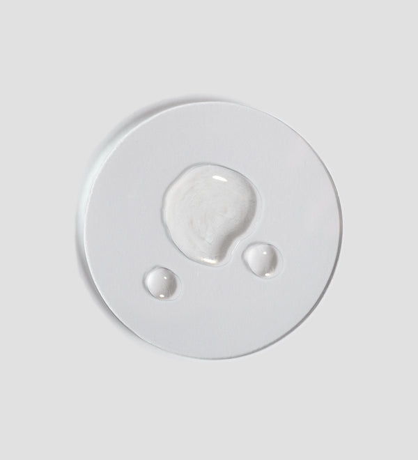 Clear liquid droplets on a white surface showcasing the texture of Tranquillity Oil (Bath & Body) | [ comfort zone ] for skincare and body care wellness.