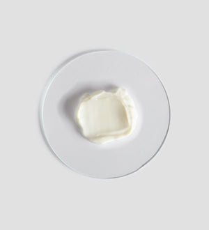 A smooth dollop of creamy white Tranquillity Body Cream | [ comfort zone ] displayed on a clear round surface, highlighting its rich texture for skincare and body care.
