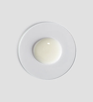 Sample of creamy white Tranquillity Shower Cream | [ comfort zone ] on a clear round dish against a light gray background, highlighting its smooth texture for skincare and body care.