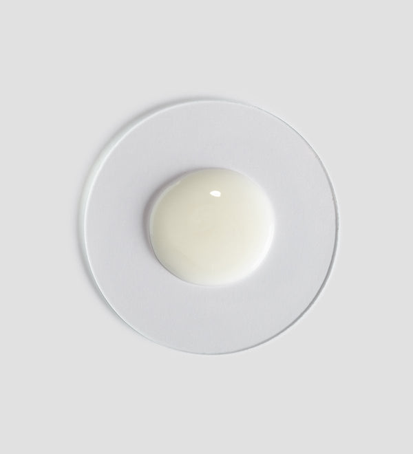 Sample of creamy white Tranquillity Shower Cream | [ comfort zone ] on a clear round dish against a light gray background, highlighting its smooth texture for skincare and body care.