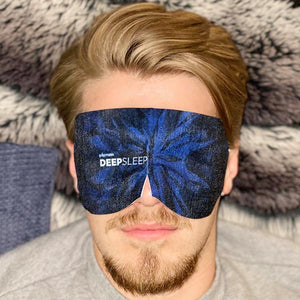 Man wearing a blue patterned Deep Sleep Fragrance-Free Self-Warming Large Sleep Mask (5 Pack) | Popmask lying on a soft textured blanket for relaxation and wellness.