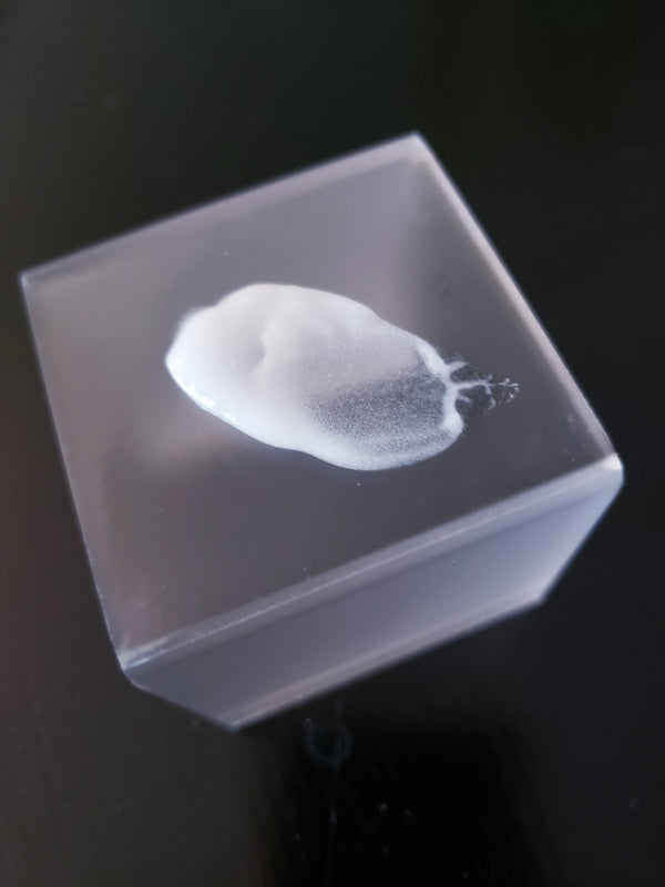Close-up of a small amount of Mild Acne Lotion with Benzoyl Peroxide | Dermatologist's Choice cream on a clear square surface, highlighting the lotion's smooth texture for skincare use.