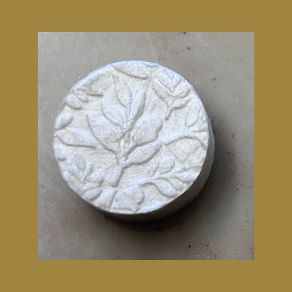Close-up of a round white makeup remover tablet with embossed botanical leaf patterns, part of the 350 Count Refill Pack Make-Up Remover | Functional Botanicals for skincare.