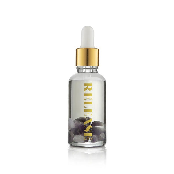 Clear glass dropper bottle with gold cap containing black stones inside labeled Release Essential Oil Vial | Aluminate Life for wellness and body care use
