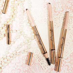 Three Defined Brilliance Dual Sided Eyebrow Pencil | Pretty Vulgar products displayed on lace and pink patterned background with pearl necklaces and gold caps.