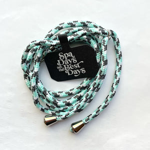 Crossbody Phone Lanyard With Adjustable Strap | Live Love Spa featuring a braided black, white, and mint green cord with metal end caps and a black tag reading Spa Days are the Best Days.