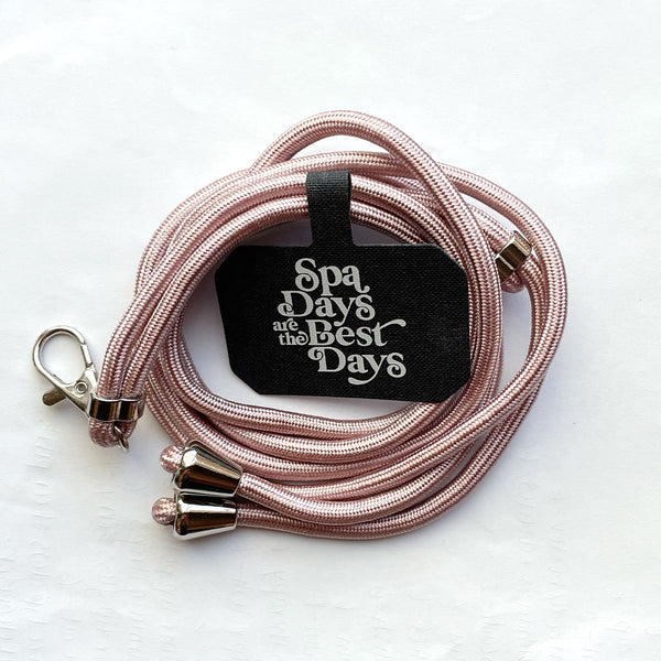 Crossbody Phone Lanyard With Adjustable Strap | Live Love Spa in soft pink with silver-tone metal clasps and a black tag that says "Spa Days are the Best Days" displayed on a white background.