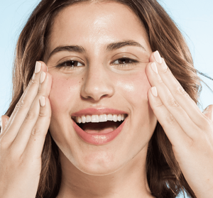 Happy woman with glowing skin gently touching her face, illustrating the effects of using Bronze Fox® Tanning Drops | Farmhouse Fresh in a skincare routine.