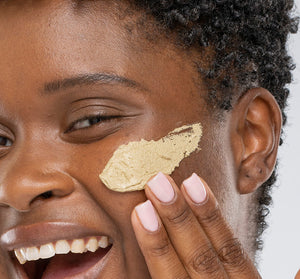 Close-up of a smiling person applying Matcha Purity™ Calm & Clear Purification Mask | FarmHouse Fresh to their cheek, showcasing skincare and self-care wellness.