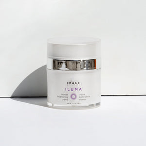 White jar of ILUMA intense brightening crème | IMAGE Skincare with silver band, placed on white surface against white background, designed for skincare and brightening.