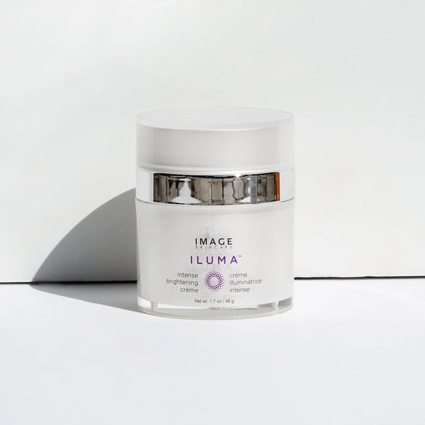 White jar of ILUMA intense brightening crème | IMAGE Skincare with silver band, placed on white surface against white background, designed for skincare and brightening.