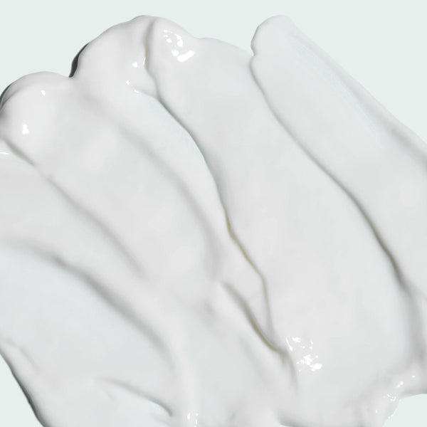 Smooth white creamy texture of ILUMA intense brightening crème | IMAGE Skincare spread on a light background, highlighting its rich skincare formula.