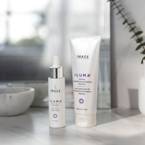 Two skincare products displayed on a marble surface with natural light, featuring ILUMA intense brightening exfoliating cleanser | IMAGE Skincare, promoting skincare and wellness.