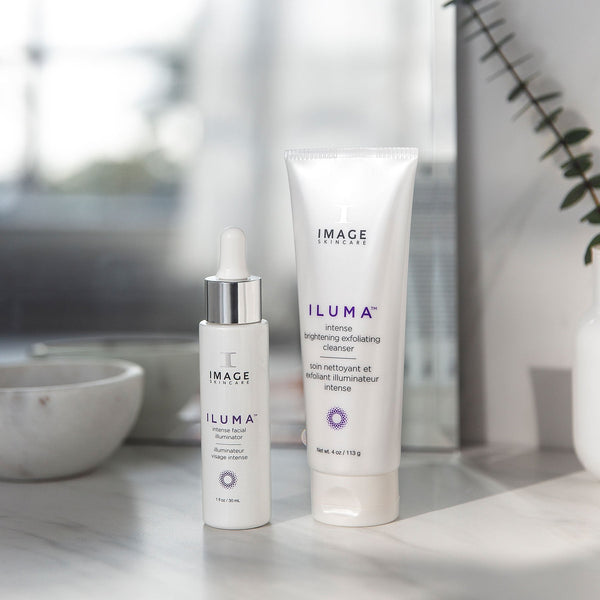 Two skincare products displayed on a marble surface with natural light, featuring ILUMA intense brightening exfoliating cleanser | IMAGE Skincare, promoting skincare and wellness.