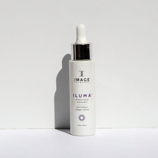 White dropper bottle of ILUMA intense facial illuminator | IMAGE Skincare standing upright on a white surface with soft shadow against a light background, highlighting skincare product packaging.