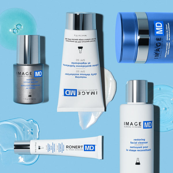 Restoring Daily Defense Moisturizer SPF 50 | IMAGE Skincare tube on blue background surrounded by related skincare products and moisturizer textures.