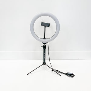 Ring Light - 10" set up on a tripod stand with a phone holder in the center and an attached power cable, against a plain white background.