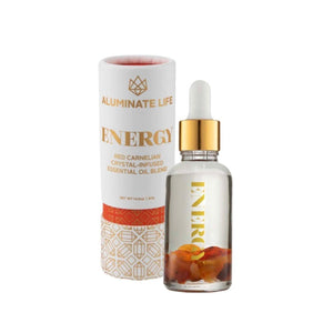 Clear glass dropper bottle with golden cap containing a crystal-infused oil blend next to a white and gold decorative cylindrical box labeled Energy Essential Oil Vial | Aluminate Life.