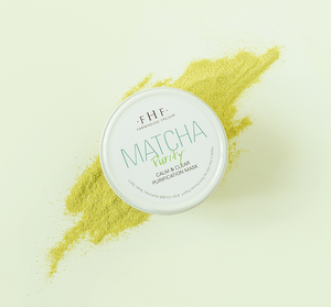 Container of Matcha Purity™ Calm & Clear Purification Mask | FarmHouse Fresh resting on a pale surface with a spread of vibrant green matcha powder behind it, highlighting skincare and wellness.