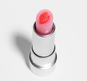 Close-up of a pink lip balm with a strawberry design on top, labeled Strawberry Mood Fruit™ Lip Therapy | Farmhouse Fresh, showcasing a skincare lip care product.