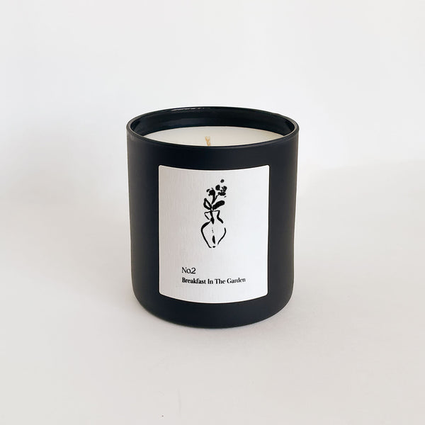Minimalist black candle container with a white label featuring a simple floral illustration, presenting the No. 2 Breakfast In The Garden (Swiss Alps) Candle | Lucky Owl.