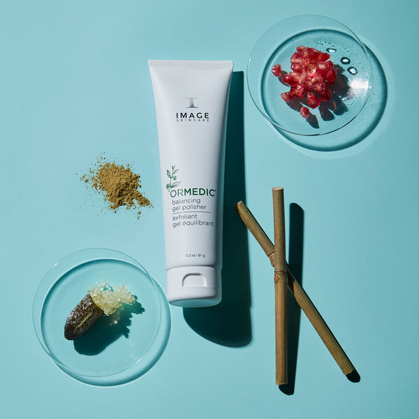 ORMEDIC balancing gel polisher | IMAGE Skincare tube surrounded by natural exfoliating ingredients and bamboo sticks on a light blue background, promoting skincare and wellness.